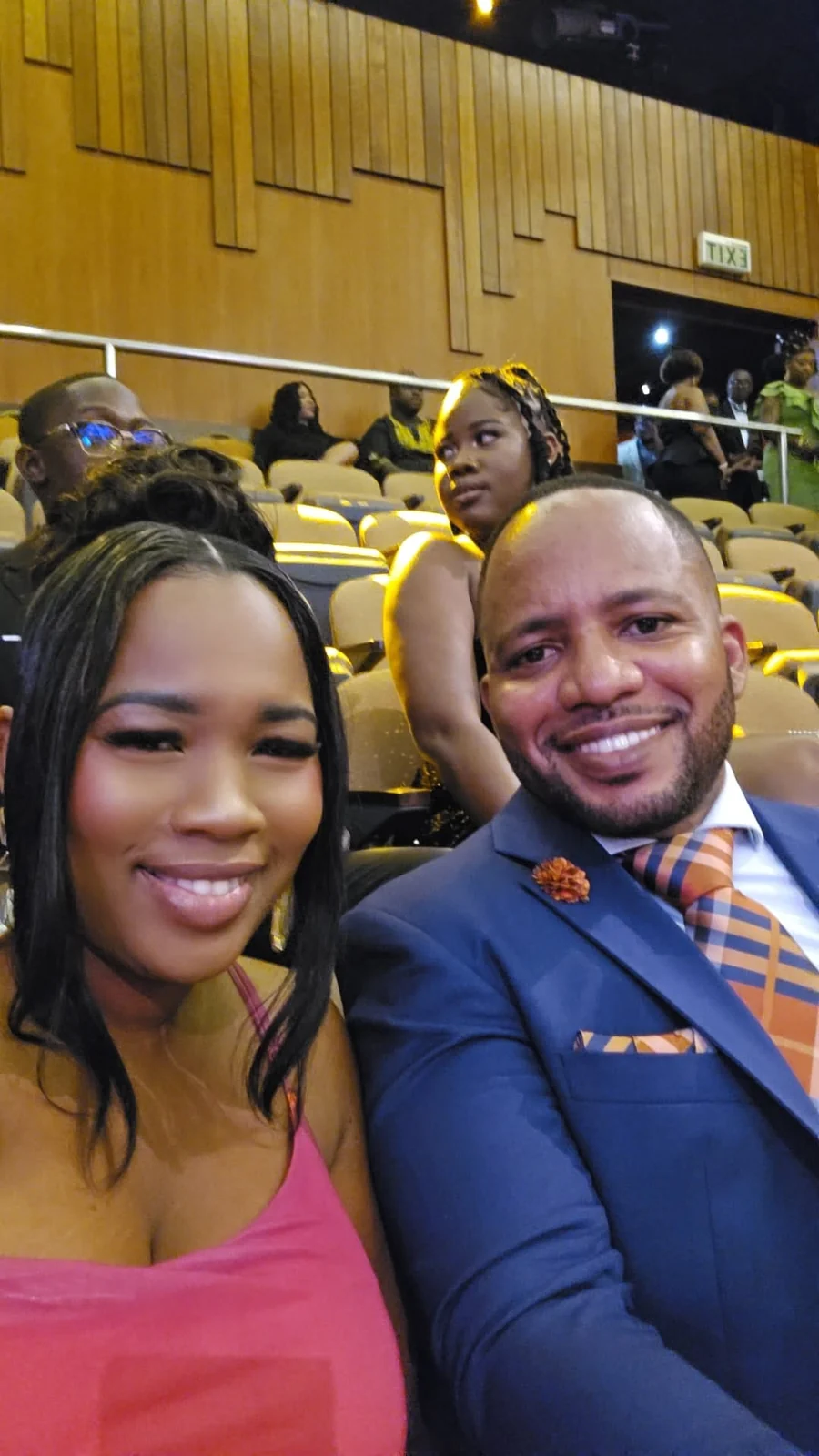 Jamar and a woman in pink taking a selfie in an auditorium